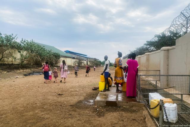 SRF bi de Lüt – HeimwehSüdsudanStrassenszene im Dorf Korok: Frauen und Kinder aus dem Ort holen Wasser vom Überlauf des Compound, der eine eigene Quelle besitzt. Auf der Strasse sind Sybille Graf und eine Nachbarin mit ihren Kindern unterwegs.2023Copyright: SRF
